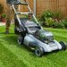 Person mowing a small green backyard with a cordless electric mower.